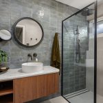 Modern bathroom design featuring a round mirror, sleek shower enclosure, wooden vanity with a vessel sink, and stylish tile accents, showcasing Cornerstone Property Group's renovation expertise.