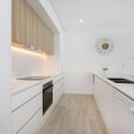 Modern kitchen featuring sleek white cabinetry, integrated appliances, and warm wood accents, showcasing a stylish renovation ideal for home transformation.