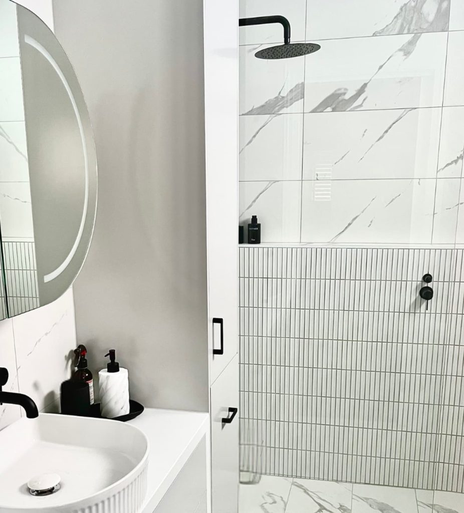 Modern bathroom design featuring a stylish sink with a round mirror, sleek black fixtures, and a spacious shower area with marble and textured tiles, showcasing the quality of Cornerstone Property Group's renovation services.