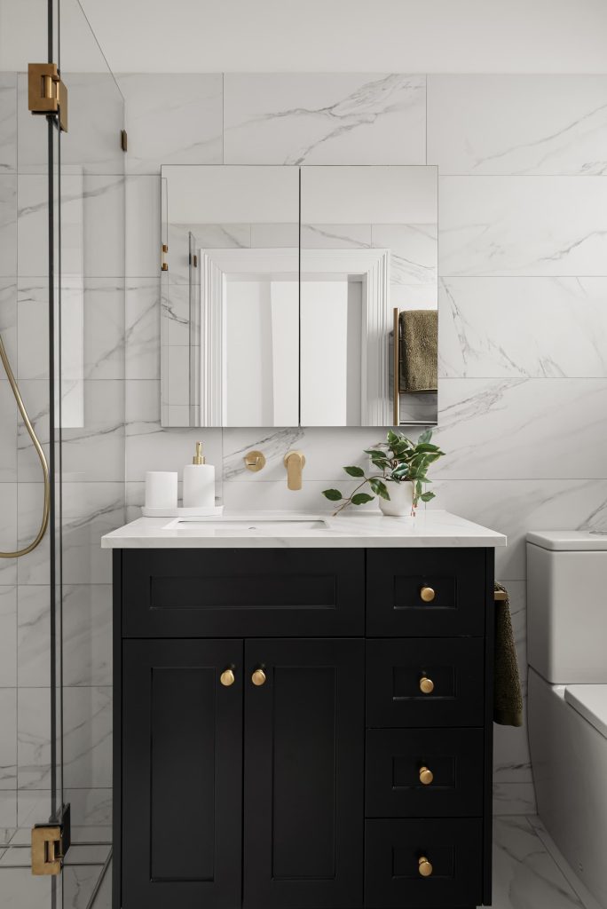 Modern bathroom renovation featuring a black vanity with gold hardware, marble tiles, a large mirror, and a potted plant, illustrating Cornerstone Property Group's design style for Surrey Hills renovations.