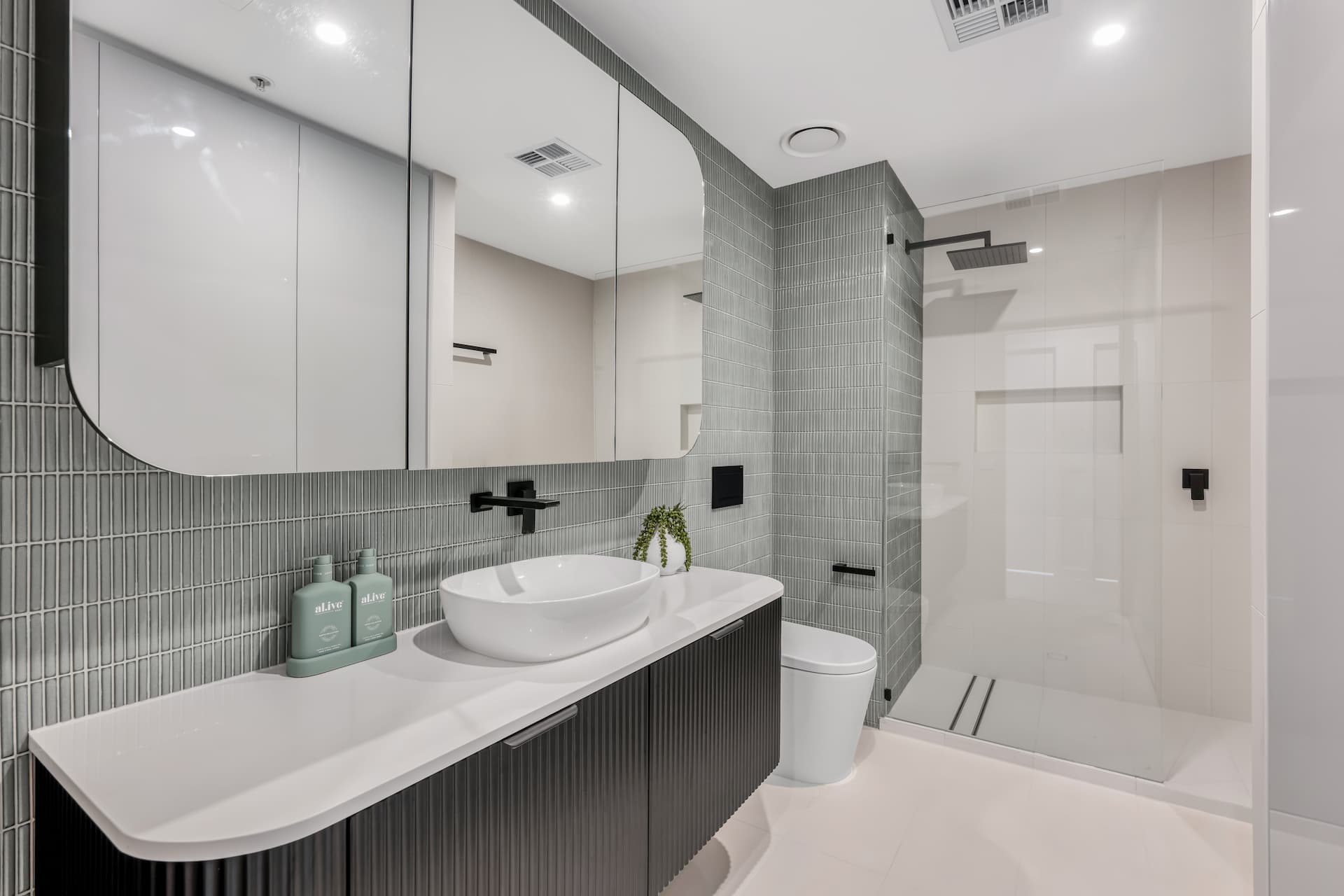 Modern bathroom design featuring a sleek black vanity, round white basin, green accent tiles, and a glass shower enclosure, illustrating contemporary renovation aesthetics relevant to bathroom renovation costs.