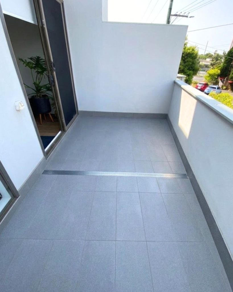 Modern balcony with gray tiled flooring and drainage system, showcasing a clean and renovated outdoor space ideal for Melbourne homes.