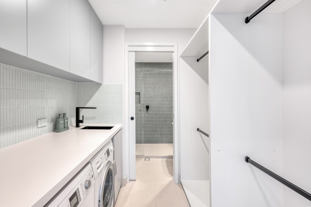 Modern laundry room design featuring white cabinetry, sleek countertop, and integrated appliances, showcasing efficient layout and functionality for home renovation.