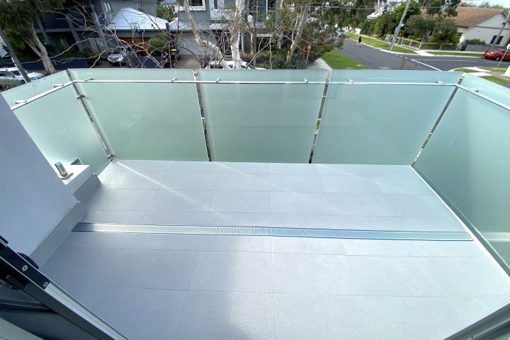 Modern balcony renovation featuring sleek glass railing and grey tiled flooring, highlighting home improvement aesthetics by Cornerstone Property Group.